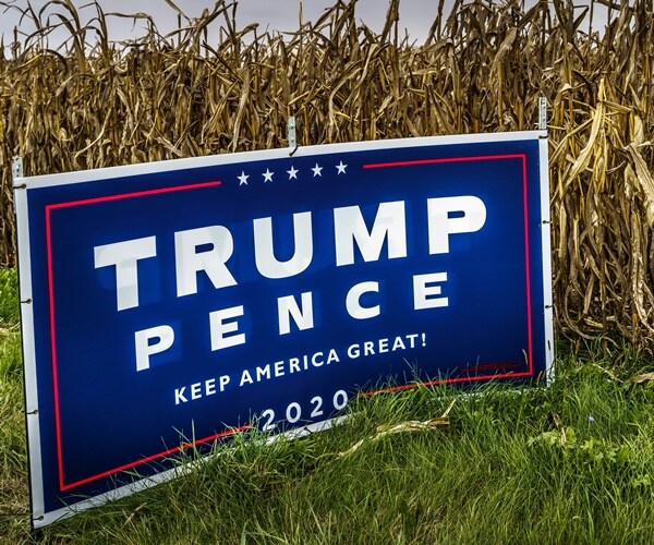 a trump-pence yard sign is next to corn stalks