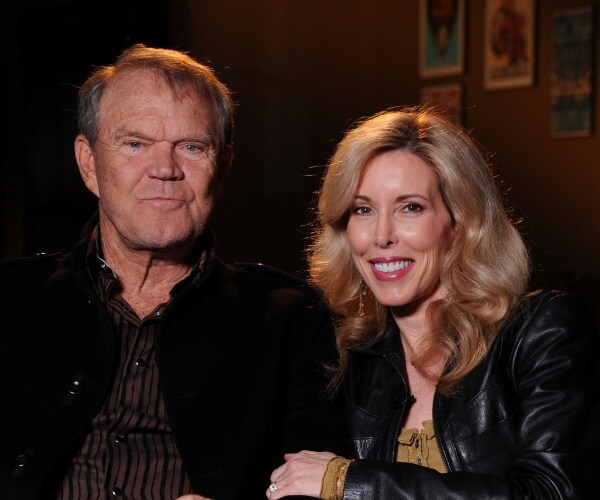 glen campbell in a black jacket and striped shirt with kim in a black leather jacket and green top