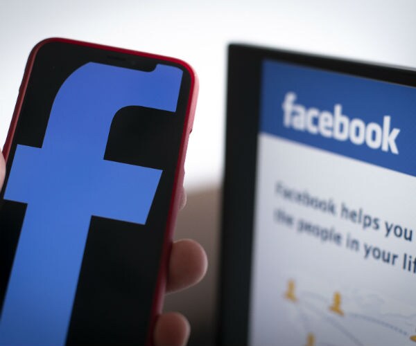 A Facebook logo is seen on a mobile device with the Facebook login screen in the background