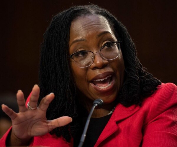 ketanji brown jackson with hand in forefront wearing glasses and red outfit