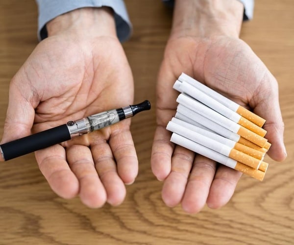 man holding cigarettes in one hand and vapes in the other