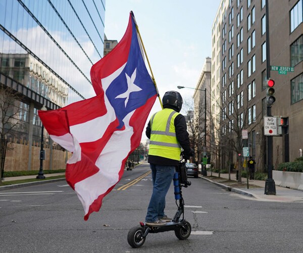 a man waving the puerto rico flag rides a scooter in washington dc
