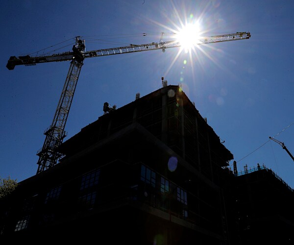 a crane stands over a building under a bright sun in seattle, the site of a deadly crane accident