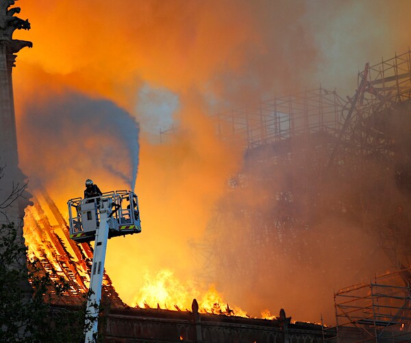 notre dame cathedral in paris is being fought by a firefighter from an elevated ladder position