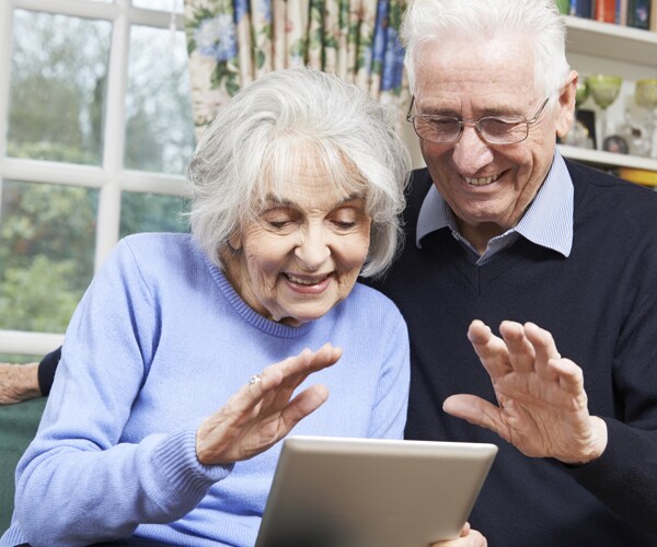 two senior citizens smiling and waving while on a video chat