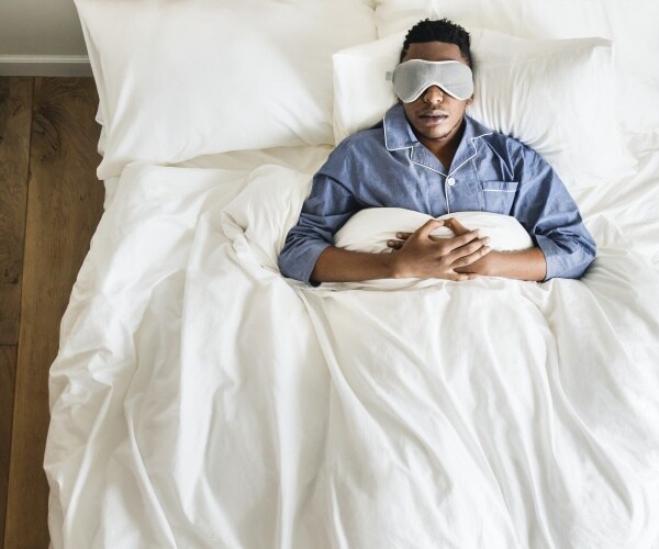 man sleeping in bed with a sleep mask over his eyes