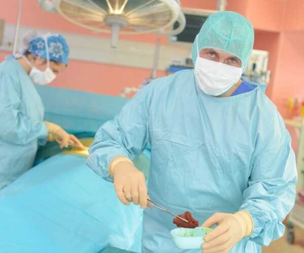surgeon in operating room removing an organ from a patient