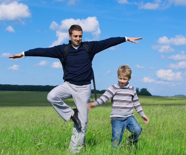 man balancing on one leg while out in a field playing with his son