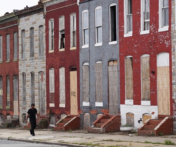 a man walks past boarded up row houses
