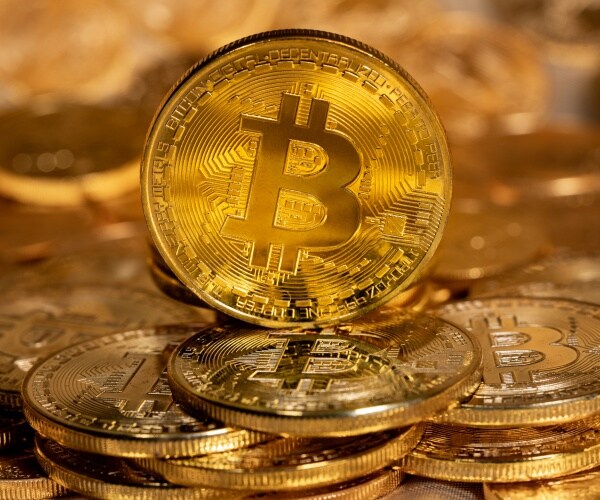Single Bitcoin coin standing on top of other gold coins