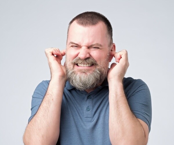 wincing man with fingers in ears due to annoying sound