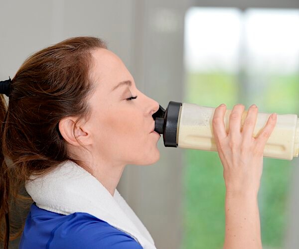 a woman tips her head back with eyes closed as she drinks a protein shake out of a shaker