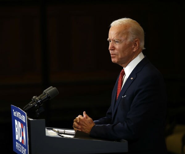 joe biden is seen speaking at a podium in a dark navy suit