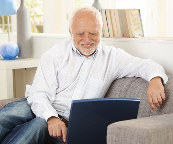 a senior man sitting on a couch and smiling at a laptop