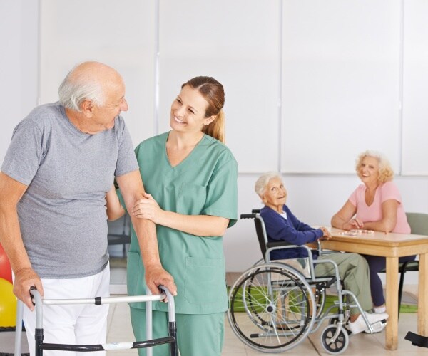 nurse helping man in nursing home, other residents in background