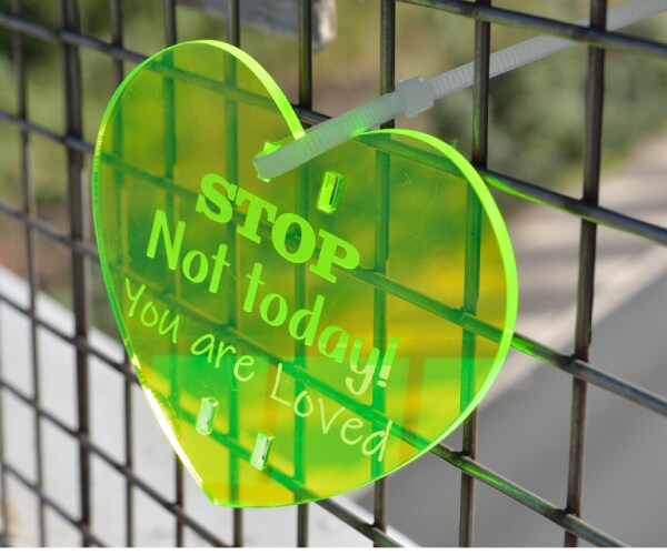 a plastic heart posted on a highway overpass reading stop not today you are loved