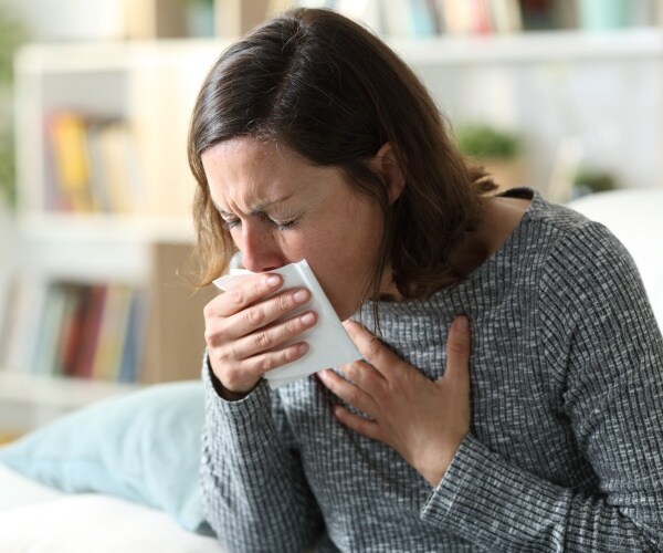 woman in a gray long sleev shirt coughs into a napkin