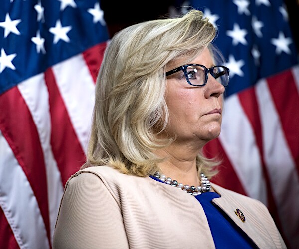 liz cheney looks to her left while listening during a news conference with american flags behind her