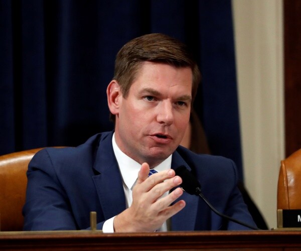 eric swalwell in a navy blue suit speaking at a hearing with one hand raised
