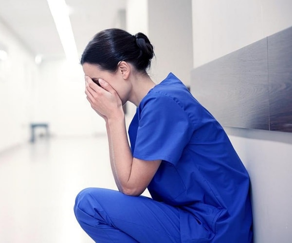 healthcare worker squatting in hall of hospital with head in hands crying