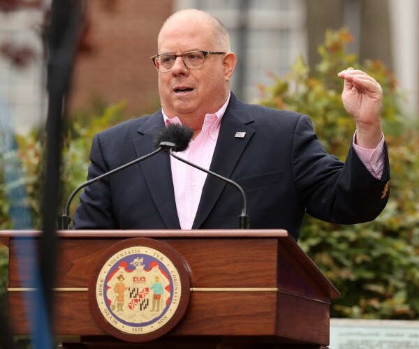 larry hogan speaks outside at a lectern with the maryland state seal on it.