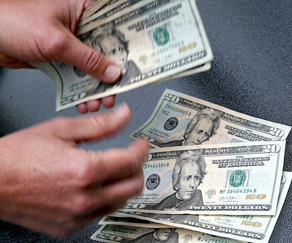 a man counts a stack of twenty dollar bills, holding them and placing each on a table as he counts