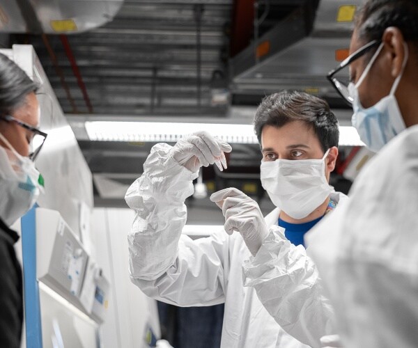 scientists in white protective suits and masks look at samples in a laboratory