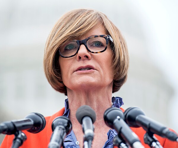 susie lee stands and speaks into a gaggle of mics during a press conference
