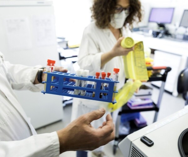 lab worker in a white coat holds up a test tube rack containing samples of covid 19