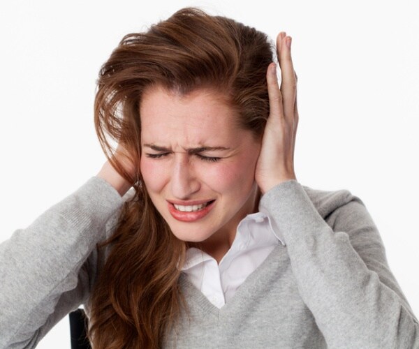 woman holds ear due to ringing in ears/tinnitus