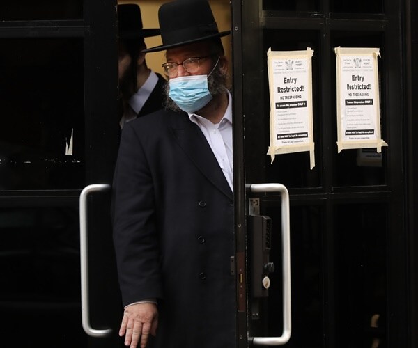 a masked hasidic man leans out of a door.