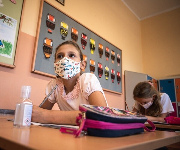 little girls wear face masks and sit in a classroom 