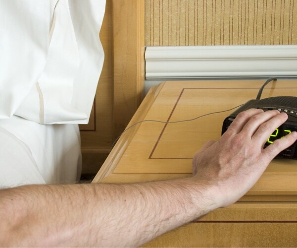 man in bed reaching out to hit snooze button on alarm clock