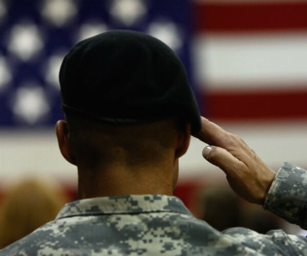 an american soldier wearing a beret and with his back to the camera, salutes the american flag with his left hand
