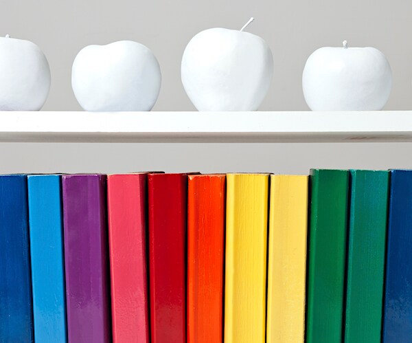 books on a book shelf are in a rainbow color with fake white apples above them on a shelf in an lgbtq  illustration