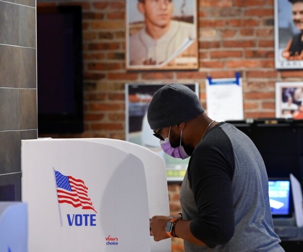 man wearing a mask votes at a booth