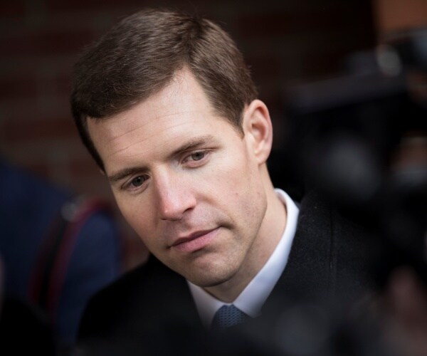 conor lamb in a black suit and blue tie looking down