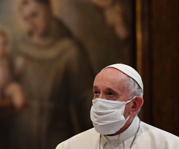 pope francis in a face mask and white robes standing in front of a painting