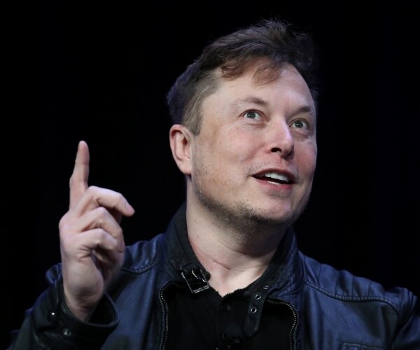 elon musk in a black leather jacket and black top pointing one finger up
