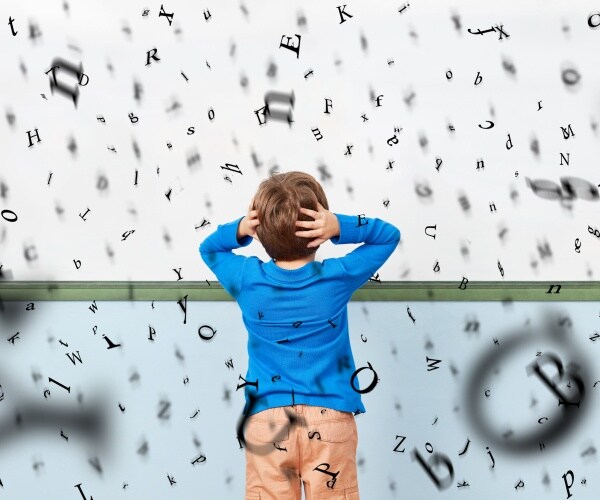 young boy at whiteboard with hands on his head as letters swirl around him