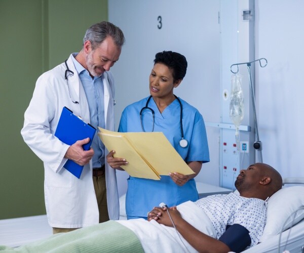 patient lies in a hospital bed with doctor and nurse standing by