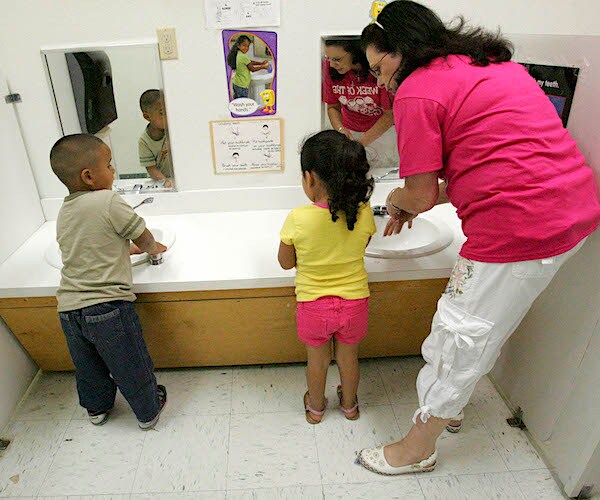 a woman shows kids how to properly wash their hands