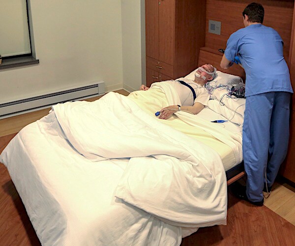 a person sleeps while a sleep test attendant dresses up the testing equipment