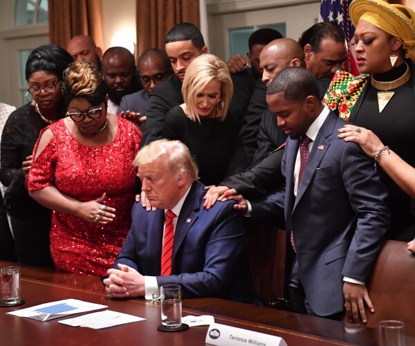 people stand over donald trump and put their hands on each other with eyes closed