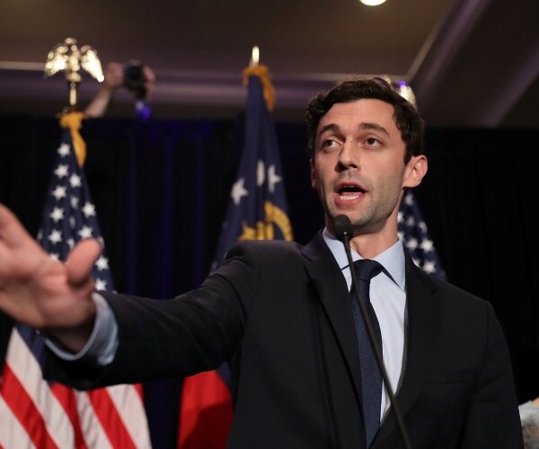 ossoff in a blue shirt and black tie in front of an american flag
