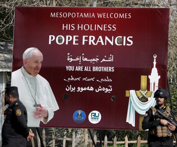 pope francis is shown on a poster in iraq with officers in uniform 