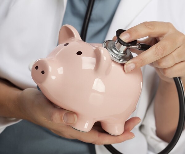 doctor examining pink piggy bank with stethoscope