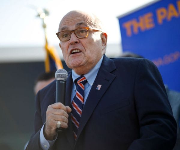rudy giuliani holds a mic and speaks during a campaign rally outdoors