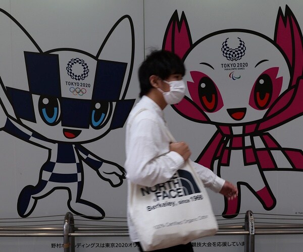man wearing face mask walks past tokyo 2020 mural