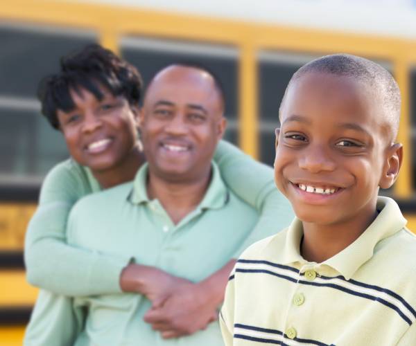 parents and a child smile in front of a school bus